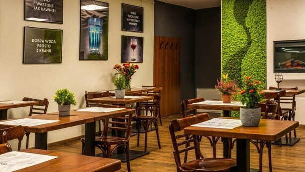 A restaurant with wooden tables and chairs, a green vertical garden wall, and framed pictures on the wall. - ParkApartamenty (Chrzanow)