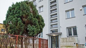 A multi-story building with a modern facade, a large tree in front, and a metal fence. - ParkApartamenty (Chrzanow)