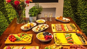 A table with various food items and drinks, including fruits, cheeses, and meats, arranged on a wooden table.