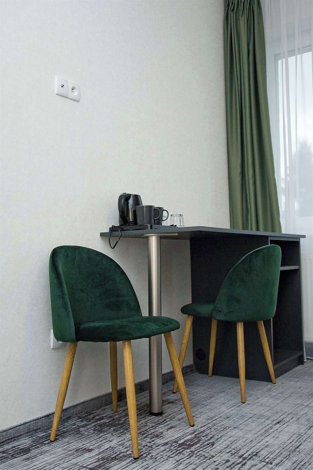 Una habitación pequeña con dos sillones tapizados en verde, una mesa de metal y una silla negra.