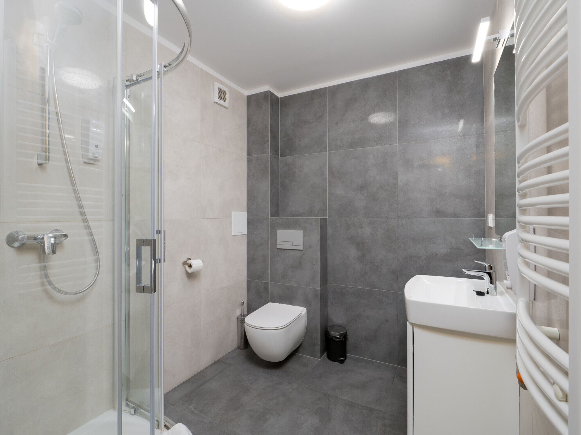 Een moderne badkamer met een glazen douchecabine, toilet en wastafel met spiegel.