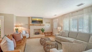 A living room with a fireplace, two sofas, a coffee table, and a large window with blinds.