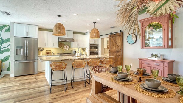 A modern kitchen with a central island, stainless steel appliances, and a dining area with a wooden table set for four.