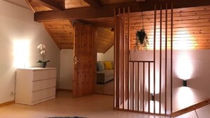 A room with a sloped ceiling, wooden beams, a white dresser, a plant, and a bed with a headboard. - Cozy Swedish Waldhof Marie - in a secluded location - fireplace & nature (Västra Götalands län)