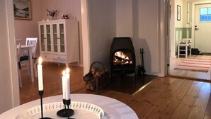 A cozy living room with a fireplace, a dining area with a white cabinet, and a view into another room. - Cozy Swedish Waldhof Marie - in a secluded location - fireplace & nature (Västra Götalands län)