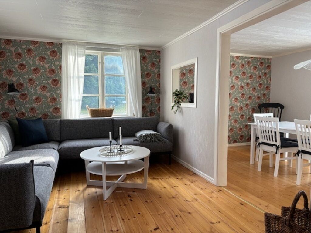 En hyggelig stue med en grå sofa, et rundt sofabord og et spiseområde med hvide stole og et bord.