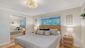 A modern bedroom with a large bed, bedside tables, a mirror, and a window with blinds.