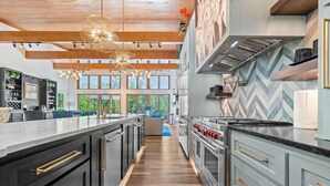 A modern kitchen with a long island, stainless steel appliances, and a herringbone tile backsplash. - Luxurious Retreat | Private Creek View | Hot Tub (Hot Springs)