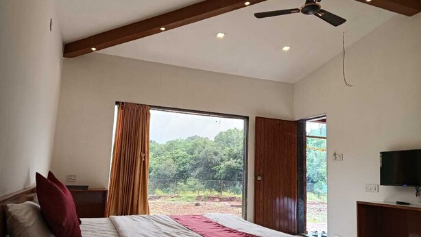Une chambre avec un grand lit, un ventilateur de plafond, une télévision et une vue sur la verdure environnante.