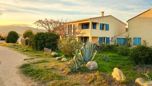 Ein zweistöckiges Haus mit blauen Fensterläden, umgeben von einem Garten mit Steinen und Kakteen.