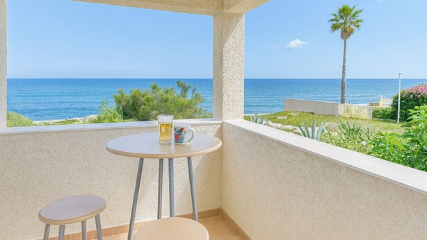 Ein Balkon mit Meerblick, ein Tisch mit Glas und Tasse sowie zwei Stühle.