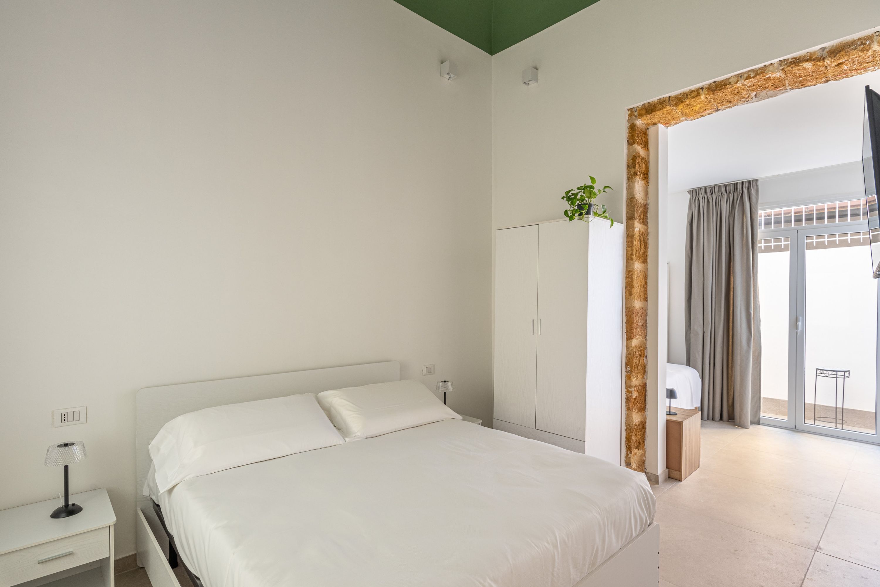 A bedroom with a bed, a nightstand, a wardrobe, and a view of the outside through a glass door.