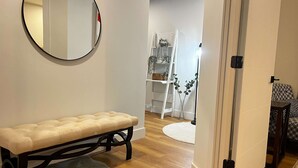 Ein Zimmer mit einem runden Spiegel, einer gepolsterten Bank, einem grauen Teppich, einer weißen Tür und einem gemusterten Sofa.