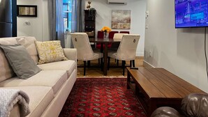 Ein Wohnzimmer mit Sofa, Sesseln, einem Couchtisch, einem Fernseher und einem Essbereich mit Tisch und Stühlen.