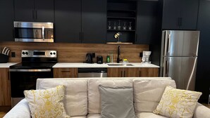 Eine moderne Küche mit dunklen Schränken, Edelstahlgeräten, einer Holz Arbeitsplatte und einem beigefarbenen Sofa mit dekorativen Kissen.