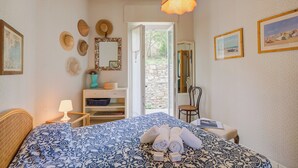 A bedroom with a bed, a nightstand, a lamp, a chair, a wardrobe, a mirror, and a door leading to a balcony. - Simply Romantic Alassio Sea View (Alassio)