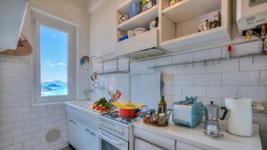 A kitchen with white cabinets, a stove, a sink, and a window with a view. - Simply Romantic Alassio Sea View (Alassio)