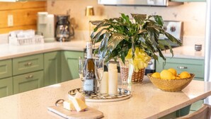 Un comptoir de cuisine avec une bouteille de vin, des verres, des bougies, une planche à découper avec du fromage, un bol de citrons et une plante en pot.