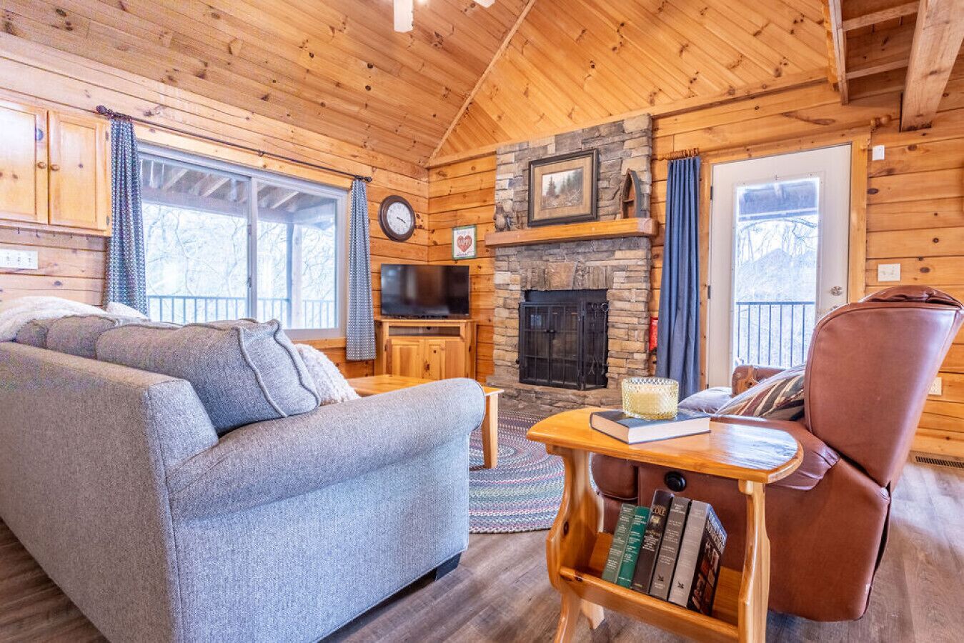 A cozy log cabin interior with a fireplace, a sofa, a chair, and a television.