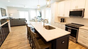 A modern kitchen with a central island, stainless steel appliances, and white cabinetry. - Three Seas 2, steps from the beach (Carolina Beach)