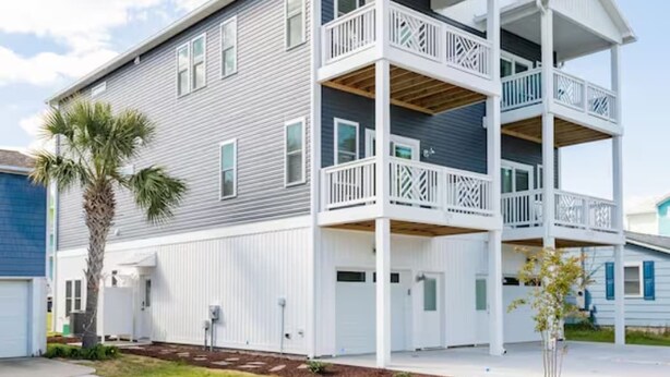 A two-story building with a balcony on the upper floor, a garage on the ground floor, and a small tree in front. - Three Seas 2, steps from the beach (Carolina Beach)