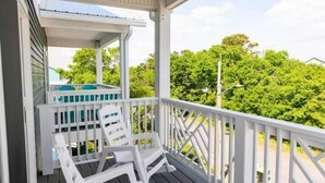 A covered porch with white railings and two white chairs. - Three Seas 2, steps from the beach (Carolina Beach)