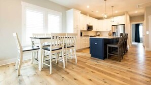 A modern kitchen with white cabinets, a central island, and a dining area with white chairs. - Three Seas 2, steps from the beach (Carolina Beach)