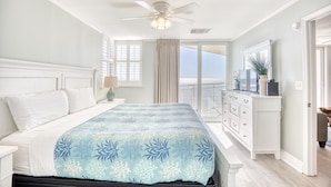 A bedroom with a bed, a ceiling fan, a dresser, and a view of the outdoors.