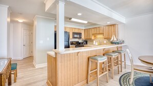 A modern kitchen with wooden cabinets, a central island with stools, and a dining area with a round table and chairs.