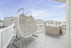 A wooden deck with a white wicker chair and a wicker sofa.