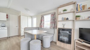 A modern living room with a sofa, ottomans, a table, a TV, and a bookshelf. - 3 Bedroom Mersea Beach Retreat-getaway by the Sea (Colchester)