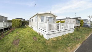 A mobile home with a fenced porch, a small deck, and a satellite dish. - 3 Bedroom Mersea Beach Retreat-getaway by the Sea (Colchester)