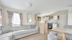 A modern living room with a sofa, a dining table, and a kitchen area with cabinets and appliances. - 3 Bedroom Mersea Beach Retreat-getaway by the Sea (Colchester)