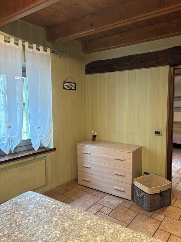 A room with a wooden dresser, a small potted plant, a sign indicating free WiFi, and a window with sheer curtains. - Rosso Mattone Mondovi (Mondovi)