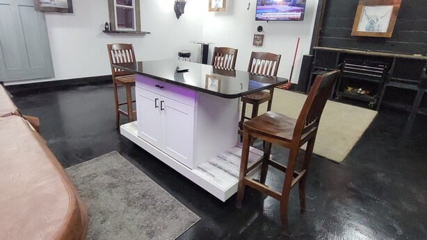 A kitchen with a bar area, wooden chairs, a white cabinet, and a television mounted on the wall.