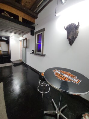 Ein Zimmer mit schwarzem Boden, einem Tisch mit Harley-Davidson-Logo, einer Stierkopf-Dekoration, einem Fenster mit blauer Beleuchtung und einer Tür mit Spiegel.