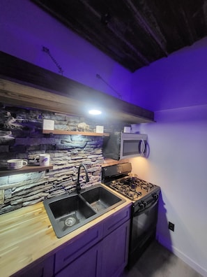 A kitchen with a stone backsplash, a sink, a stove, and a microwave.