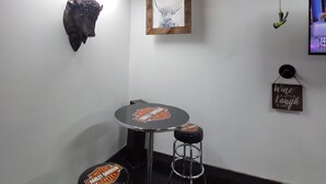 A room with a round table, two bar stools, a mounted bull head, a framed picture, and a hanging light fixture.