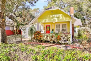 Une maison jaune avec une porte rouge, entourée d’arbres et d’un jardin.