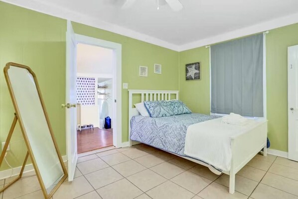 A bedroom with a bed, a door, and a view into another room.