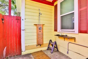 Un bâtiment jaune avec une échelle en bois, une rampe métallique et une fenêtre avec des volets rouges.