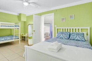 Ein Zimmer mit Etagenbetten, einem Einzelbett mit gemusterten Bettbezügen, einem weißen Schminktisch und einem Deckenventilator.