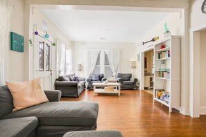 A living room with a grey sofa, a coffee table, and a bookshelf filled with books. - Spacious Home with Bikes, Near Historic Downtown (St. Augustine)