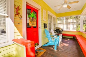 Eine Veranda mit roter Tür, Deckenventilator und einer Holzterrasse.