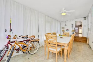 Ein Essbereich mit Tisch und Stühlen, einem Deckenventilator und Fahrrädern, die an der Wand lehnen.