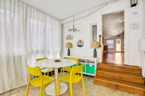 A dining area with a round table and yellow chairs, a staircase leading to another room, and a wall with a lamp and a sign.
