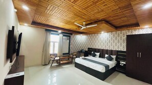 A bedroom with a bed, a desk, a chair, a wardrobe, and a ceiling fan. - Hotel Ram Janki Palace (Pindra)