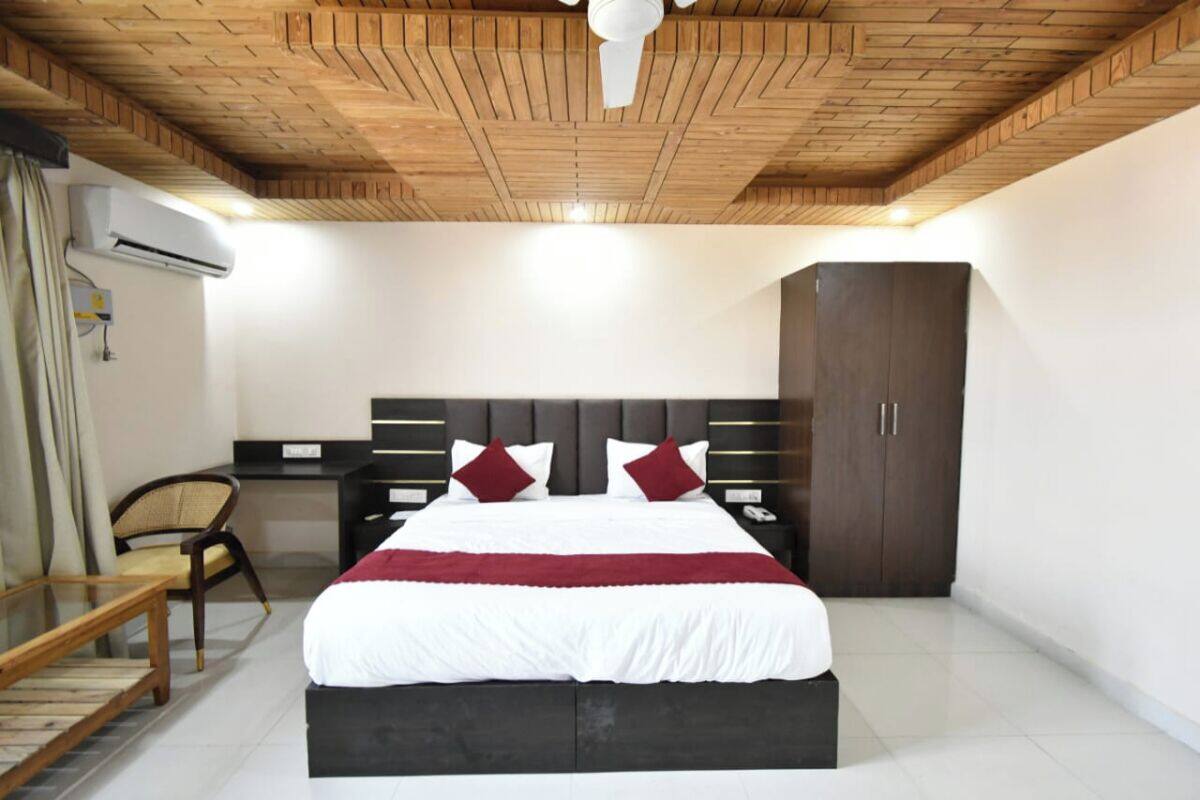 Une chambre avec un plafond en bois, un lit avec une literie blanche et rouge, un bureau avec une chaise et une armoire.