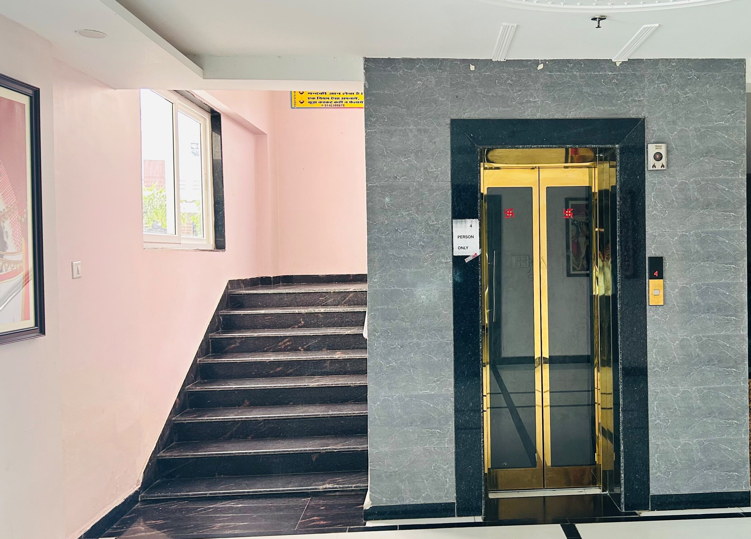 A hotel entrance with a marble wall, a staircase, and an elevator.