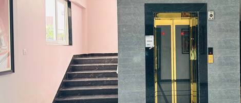 A hotel entrance with a marble wall, a staircase, and an elevator.